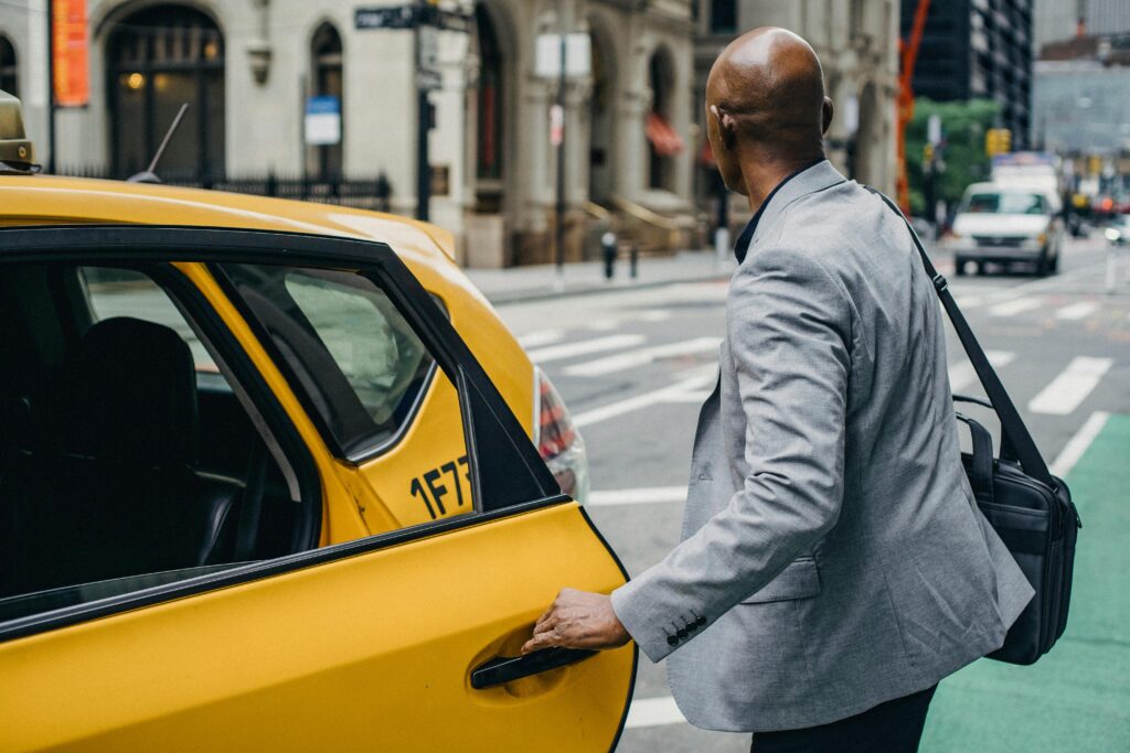 pexels-photo-5648413-5648413 A businessman in a gray suit opens the door of a yellow taxi on a bustling city street, ready for his daily commute.